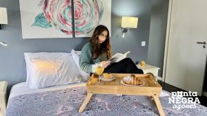 a woman sitting on a bed reading a magazine at Recanto das 5 by PontaNegraAzores in Cinco Ribeiras