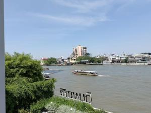 a boat on a river with a city in the background at The Quarter Chaophraya by UHG - Riverfront Hotel, Walk to ICONSIAM in Bangkok