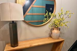 a mirror and a lamp on a wooden shelf with flowers at Modern Queen Apartment At The Victorian Unit E in Muskegon