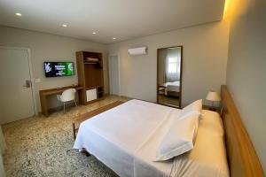 a bedroom with a large white bed and a television at Santorini Hotel - HOTEL COM ELEVADOR in Guanhães