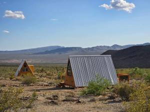 two houses in a field with mountains in the background at Starwalk Modern A-Frame #1 in Meadview