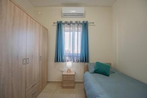 a bedroom with a bed and a window with blue curtains at The Terrace in Xgħajra