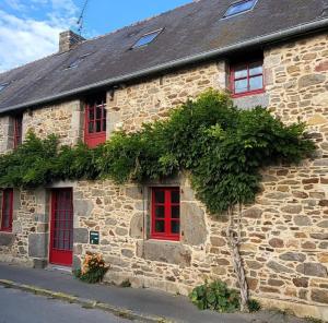 an old stone building with red windows and vegetation at Les 3 Nuances in Saint-Suliac