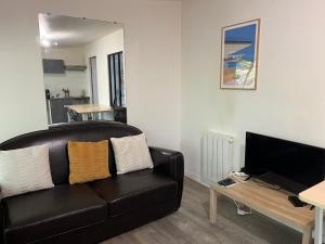 a living room with a black leather couch and a television at T2 Côté Jardin in Eysines