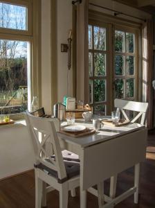 a dining room table with white chairs and windows at B&B Saense huisje in Assendelft