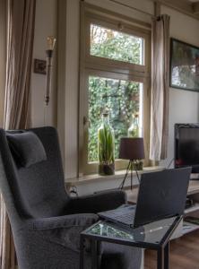 a living room with a chair and a laptop on a glass table at B&B Saense huisje in Assendelft