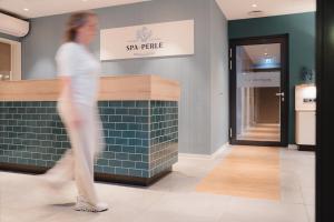a woman walking through a store with a tile wall at Küstenperle Strandhotel & Spa in Büsum +110 photos