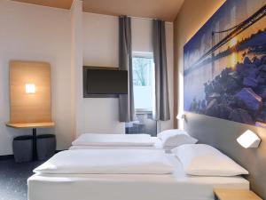 a row of four beds in a room with a tv at B&B Hotel Krefeld-City in Krefeld