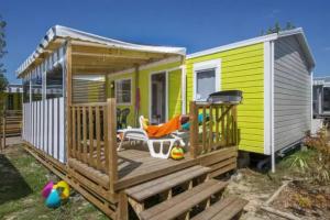 a small yellow house with a deck with a chair at Camping 5 étoiles - Parc aquatique - eecdae in Saint-Jean-dʼOrbetiers