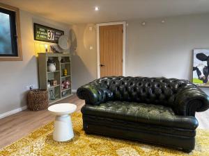 a living room with a black leather couch and a white stool at The Cabin in St. Ives