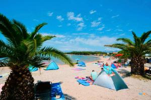 a beach with palm trees and people on the sand at Apartmani Benedetti in Povljana