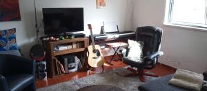 a living room with a guitar and a chair and a television at Quarto no Sótão in Coruche