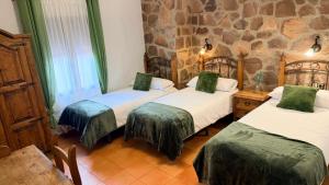 two beds in a room with a stone wall at Hotel Rural La Posada de Lía in Berzocana