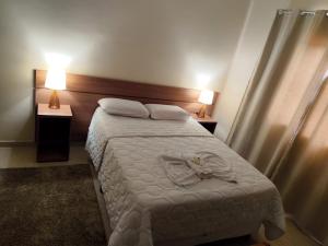 a bedroom with a white bed with two nightstands and two lamps at Paramirim Palace Hotel in Paramirim