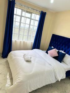 a large white bed with blue curtains and a window at Executive two bedroom embu by Tsparks in Meru