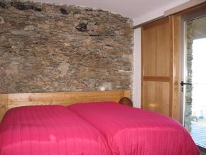a pink bed in a room with a stone wall at Quinta dos Castanheiros - Turismo Rural in Negreda