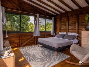 a bedroom with a bed and a chair and windows at Bungalow en duplex avec Jacuzzi in Sainte-Rose