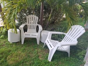 three white chairs sitting in the grass near a palm tree at Just in paradise in Baie Nettle