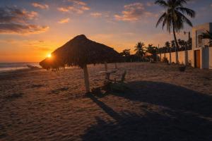 a straw umbrella on the beach with the sunset at Habitación en villa Costa del sol in Los Blancos