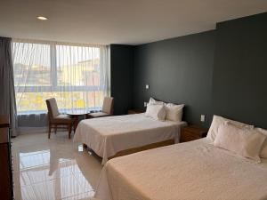 a hotel room with two beds and a table and a window at Hotel Concordia in Guadalajara
