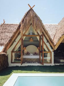 a bedroom in a straw roofed house with a pool at Vibes Villas Siargao in General Luna