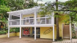 a yellow house with a white porch and a surfboard at Luxury Pearl Beach House with Private Heated Mineral Pool, Yoga Deck & Fire Pit in Pearl Beach