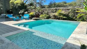 a swimming pool with blue chairs next to a house at Luxury Pearl Beach House with Private Heated Mineral Pool, Yoga Deck & Fire Pit in Pearl Beach