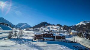 un complexe dans la neige avec des montagnes en arrière-plan dans l'établissement Hotel Gemma- Adults only, à Hirschegg