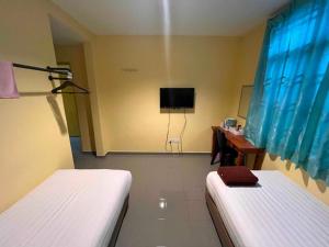 a room with two beds and a desk and a television at Kemas Homestay in Johor Bahru