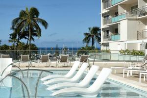 a swimming pool with white chairs and a building at Ilikai Hotel Condo with Kitchen and Ocean View in Honolulu