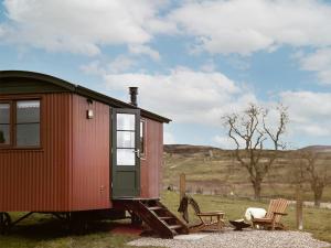 a red tiny house with a chair and a table at Lapwing Shepherds Hut - Uk7631 in Pitlochry