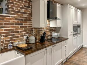 a kitchen with white cabinets and a brick wall at Coachmans Cottage in Settle