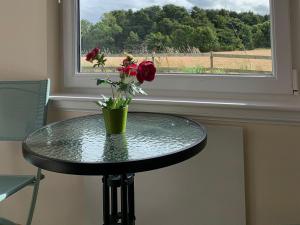 a table with a vase with roses on it in front of a window at Ploughmans Cottage-Uk7346 in Dyke