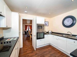 a kitchen with white cabinets and a clock on the wall at The Osprey-Ukc5062 in Aviemore