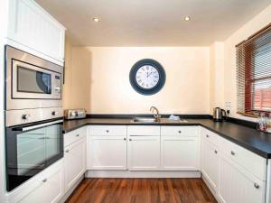 a kitchen with white cabinets and a clock on the wall at The Osprey-Ukc5062 in Aviemore