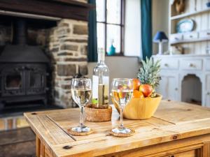 two wine glasses on a wooden table with a bottle of wine at Jasmine Cottage - Ukc4694 in Kilkhampton