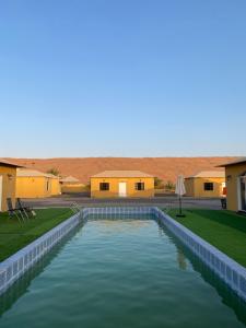 ein Pool inmitten eines Gartens mit Häusern in der Unterkunft Sand Camp Oman in Badīyah