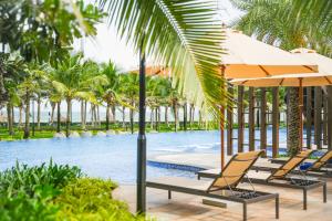 a pool with chairs and umbrellas and palm trees at Costamigo Phan Thiet, BW Premier Collection in Phan Thiet