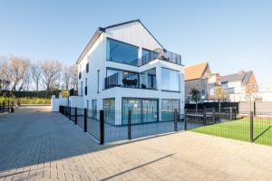 a white house with a fence in front of it at Luxury Apartment with 4 Rooms, Pool and Modern Comfort in De Haan