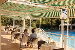 two people sitting at tables on a patio near a pool at Hotel Sierra Silvana in Selva di Fasano