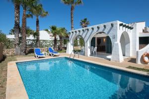 a swimming pool with two blue chairs and palm trees at Villa Flor by 3VILLAS in Cala en Bosc
