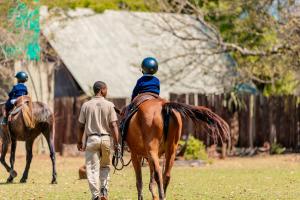 two people riding on the backs of horses in a field at Mlilwane Game Sanctuary in Lobamba