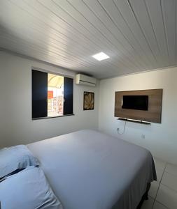 a bedroom with a white bed and a flat screen tv at Studio luxo Periperi in Salvador