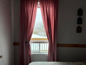 a bedroom with a window with red curtains and a bed at Gite La Ptite Falaise hébergement touristique et appartement in Sainte-Anne-des-Monts