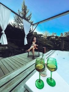 a woman sitting on a deck with two glasses of wine at Cabañas Ecologe BLESS in Chiquinquirá