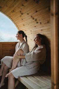 zwei Frauen sitzen auf einer Bank in einer Sauna in der Unterkunft Osada Augustów in Mirsk