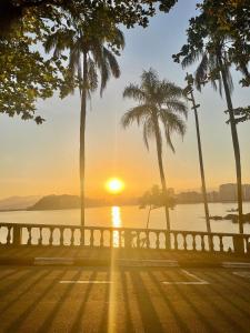 a sunset over the water with palm trees at Flat Romance Praia e Home Office in São Vicente