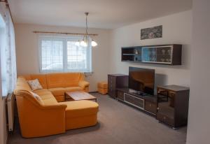 a living room with an orange couch and a tv at Apartmán se společným bazénem Zlonice in Zlonice