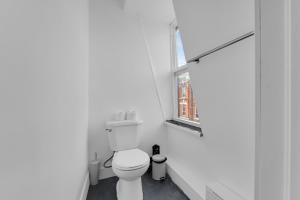 a white bathroom with a toilet and a window at Guestic Hotel at Queen West in Toronto