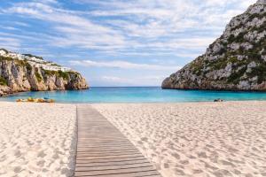 a beach with a wooden pathway leading to the ocean at EcoHome Menorca in Cala en Porter